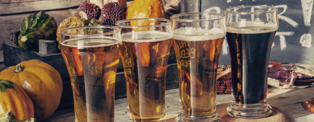 Pints of beer in front of seasonal fall vegetables.