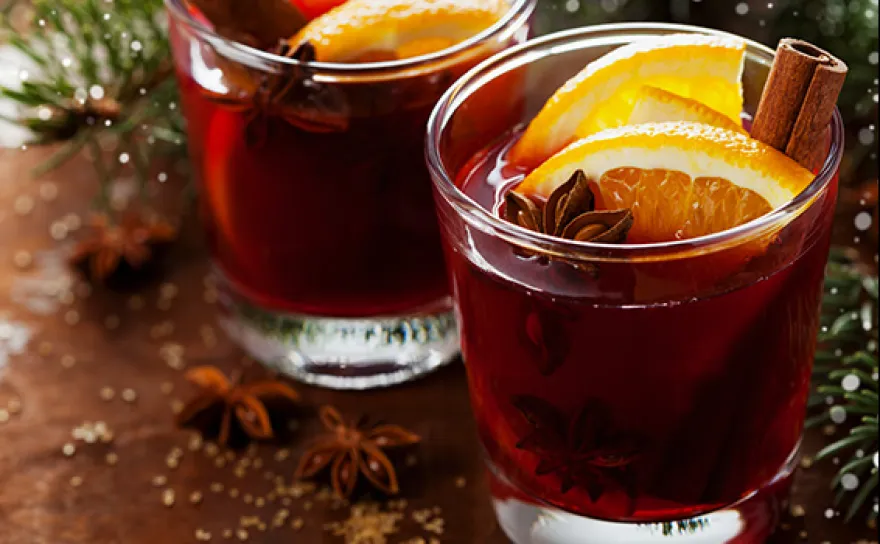 Glasses of deep red spiced beverages with orange slices in them.