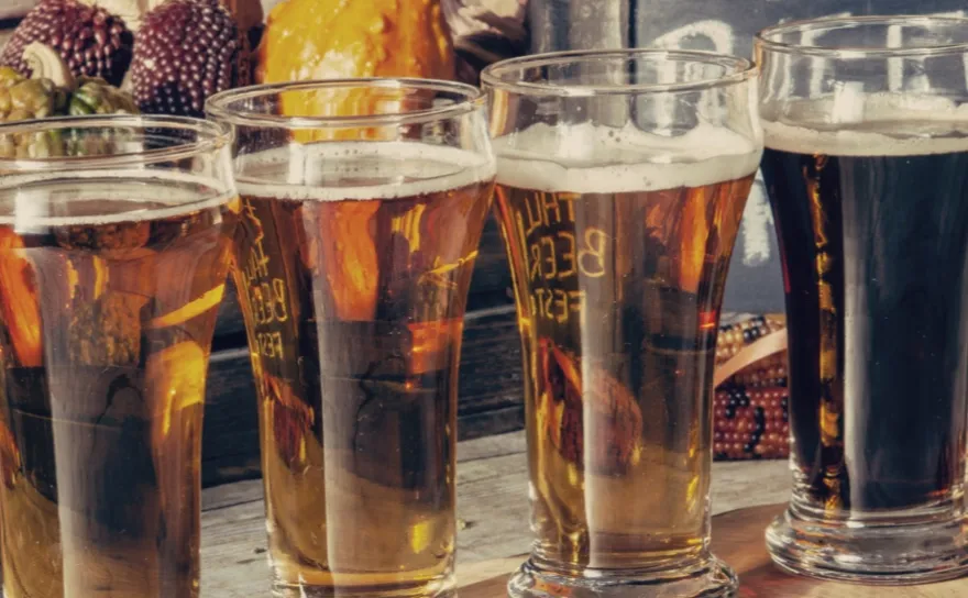 Pints of beer in front of seasonal fall vegetables.
