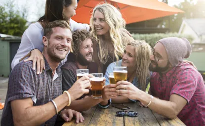 A group of people smiling and clinking their beer glasses at a picnic table