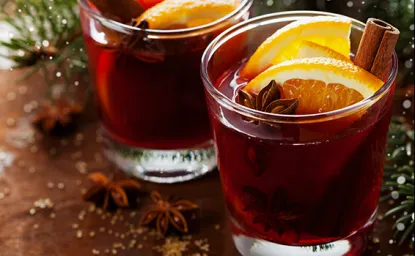 Glasses of deep red spiced beverages with orange slices in them.