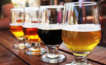 closeup photo of four glasses of beer of varying colors aligned atop a dark wooden bar