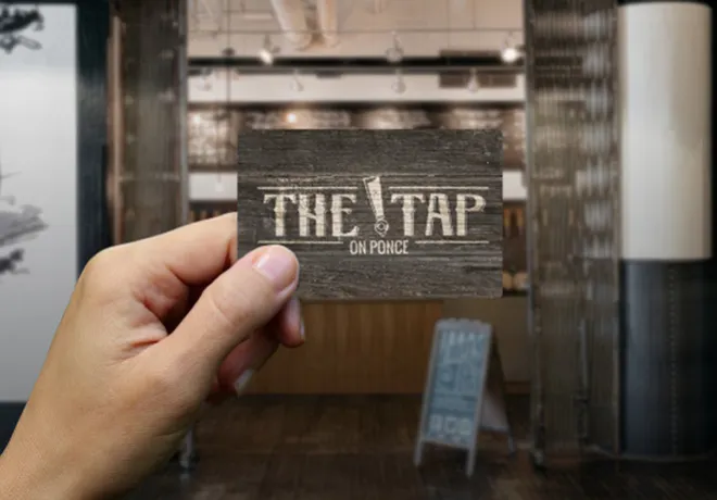Hand holding up a brown gift card with The Tap logo on it.